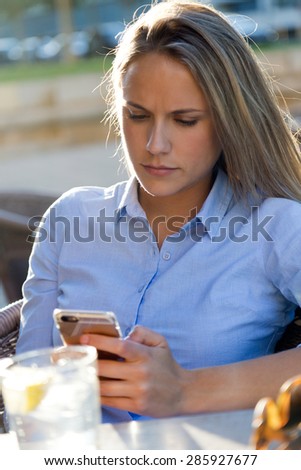 Portrait of beautiful young woman using her mobile phone in a restaurant terrace.