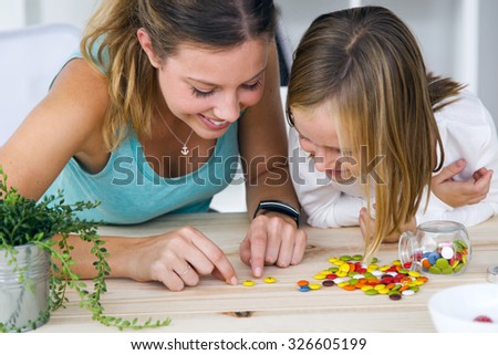 Portrait of young mother and daughter playing with sweets at home.