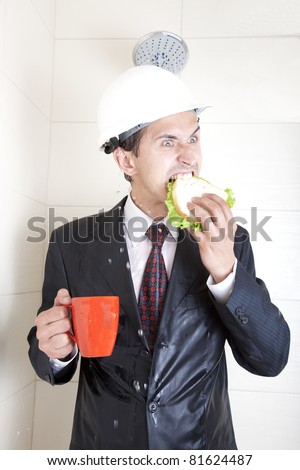 adult young businessman at breakfast in the shower in a business suit and helmet. eating sandwich and drinking from red cups