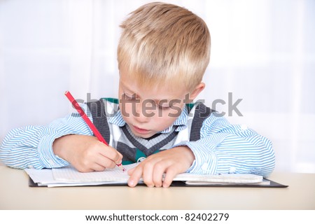 schoolboy sitting at a desk with a notebook and pencil and write. portrait, close up