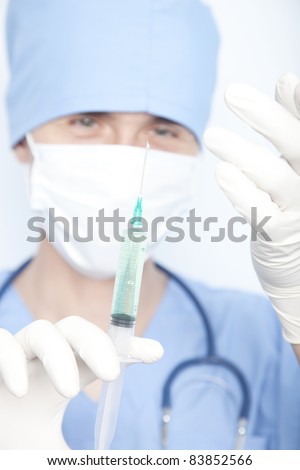 doctor in a mask with a syringe in his hand and a green liquid in the syringe. touch the needle with gloves on