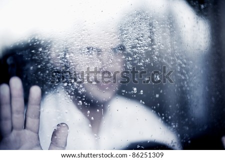 photo of young adult man standing at the window on a rainy day. focus on the raindrops on the glass. toned image