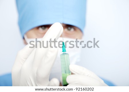 doctor in a mask with a syringe in his hand and a green liquid in the syringe. touch the needle with gloves on