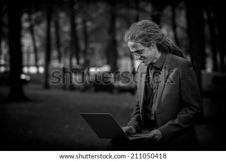 Business man with long dreadlocks working on a laptop in the open air, smiling at his computer
