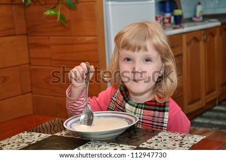 Three year old girl is eating porridge for breakfast