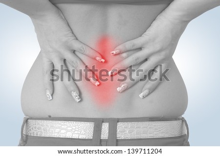 Acute pain in a woman back. Female from behind holding hand to spot of back pain. Concept photo with read spot indicating location of the pain. Isolation on a white background.