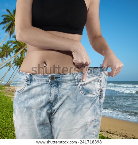 Woman shows her weight loss by wearing an old jeans, isolated on white background
