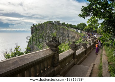 BALI - APRIL 12, 2014: Tourists climb the steps up the cliff to reach an ancient temple at the top in Uluwatu, Bali Island. The famous Balinese dance \'kecak\' performed here is a tourist attraction.