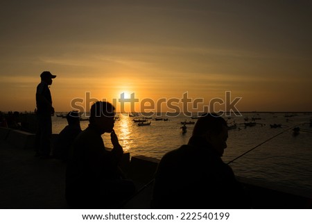 silhouettes people fishing, against the sea filled with fishing boats at sunset in Bali.