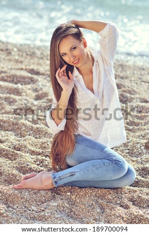 The attractive bright girl sits on the bank of a beach smiles