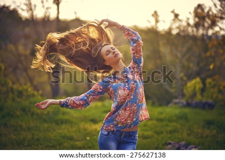 Beauty Girl Outdoors enjoying nature. Beautiful Teenage Model girl with long healthy blowing hair running on the Spring Field, Sun Light. Glow Sun. Free Happy Woman. Toned in warm colors