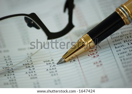Financial report with reading glasses and golden pen - focus on the pen and figures on magazine