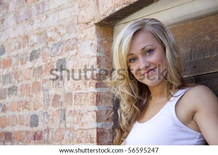 A young woman stands in a doorway, smiling at the camera. Lots of negative space on the brick wall to the left, perfect for your text.