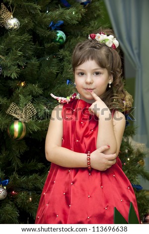 little girl in the strawberry dress costs near the decorated fur-tree and waits for a gift