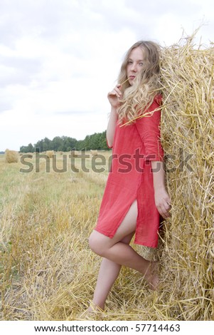 The woman in a red dress costs near a stack of straw and holds in a mouth a straw
