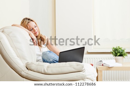 Pretty pensive young woman sitting on white couch with laptop computer