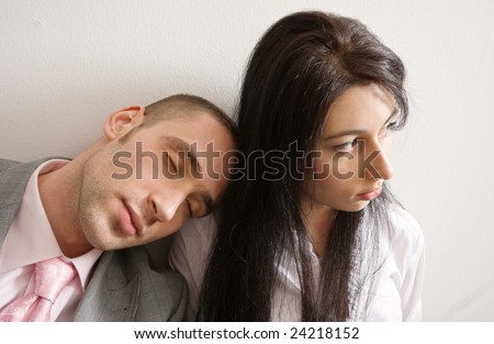 Young man and woman leaning against the wall; man is sleeping on woman\'s shoulder