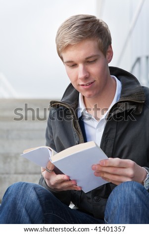 Young cheerful handsome guy reading a book with blank cover