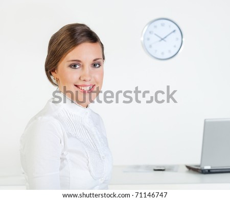 Young pretty smiling businesswoman standing in front of her desk in the office