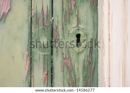 Keyhole in an old wooden door with green paint peeling off from age