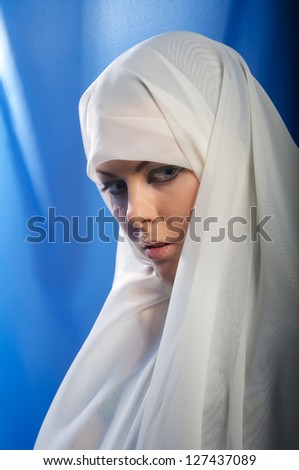 sad girl in white hijab looks down on blue background