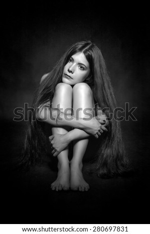 sad young naked woman with long hair sitting in dark monochrome