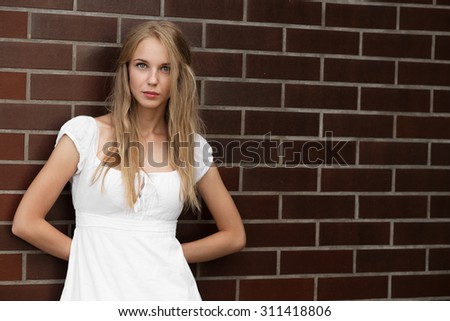 serious blond young woman near bricks wall, image with copyspace