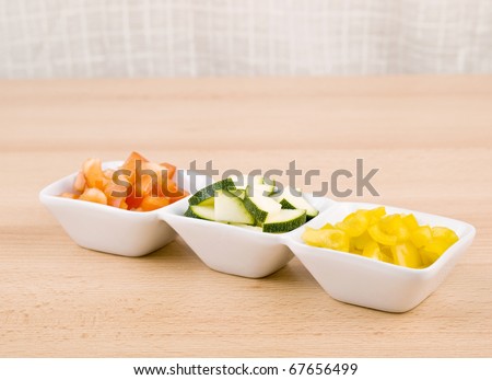 Fresh paprika and zucchini in small porcelain bowls on wooden table