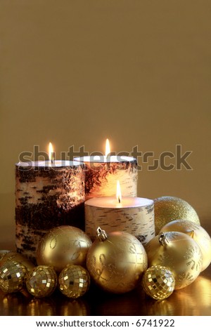 Golden Glow (vertical): A trio of candles glows warmly amongst glittering gold ornaments against a reflective gold background. Space for copy. Holiday concept.