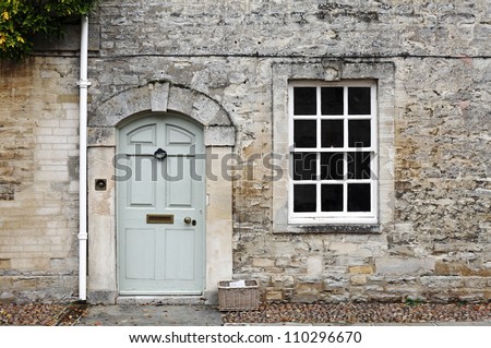 A vintage door and window on the facade of an old English cottage stone wall.