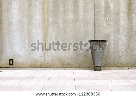 Sidewalk along a stained grungy concrete panel wall with a metal rubbish bin.