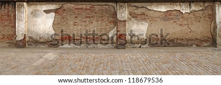 A panoramic stretch of damaged grungy red clay brick wall along a cobble stone sidewalk.