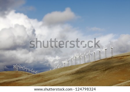 Energy wind farm with rows of giant windmill on top of a hill against a dramatic cloudy sky.
