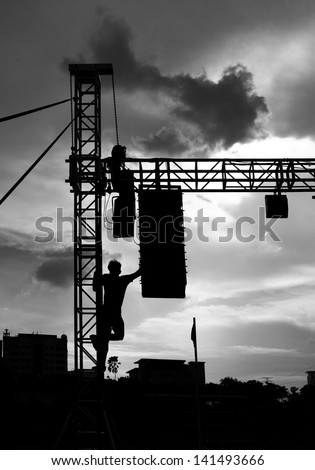 Silhouette of a sound technician climbing a concert stage equipment frame on a concert stage.