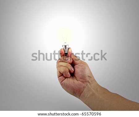 An isolated hand holding a lighted incandescent light bulb between the thumb and index finger which illuminates the area.