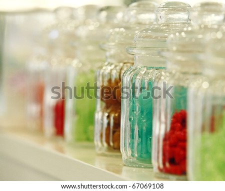 A row of transparent glass jars of tasty colorful jelly beans.