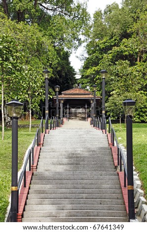 An image of a long concrete stairway to a rustic gateway into a green park.