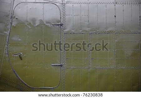 A grungy metal surface of an army airplane with an access door covered with rivets as textural background.