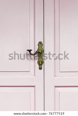 A decorative vintage brass door handle on a pink color timber panel door.