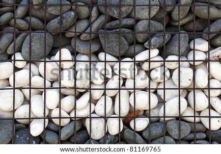 Exotic black and white river pebble stack in a metal cage for textural background.