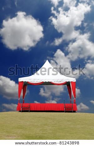 A colorful and cheerful outdoor performance stage with a tent, on a green grassy field against a blue cloudy summer sky.