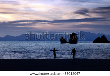 Silhouette of a lady dancing while being photographed by a photographer on a coastal beach in Langkawi Island, during a candy colored surreal sunset.