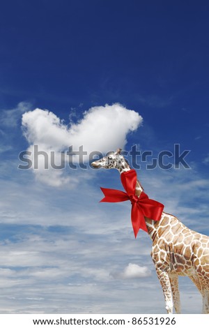 A tall giraffe with a red ribbon bow tied around its neck against a blue cloudy sky.