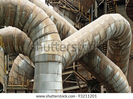 Rusty exhaust pipe of an industrial manufacturing pipe meandering and curving around in an intricate pattern.