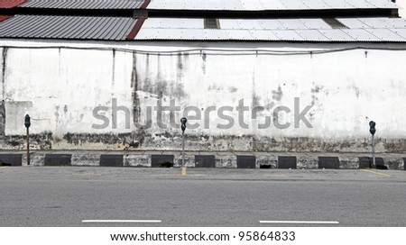 Parking spaces with parking meters by a grungy wall along an empty road.