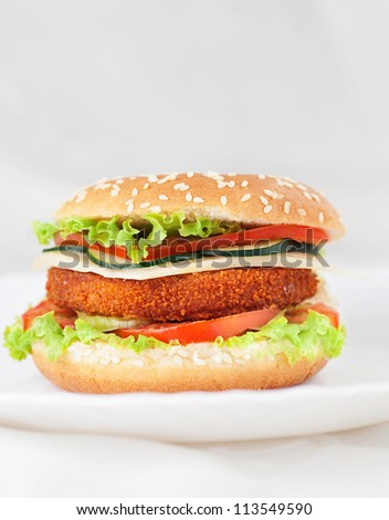 Junk food concept. Deep fried chicken or fish burger sandwich with lettuce, tomato, cheese and cucumber on wooden background.