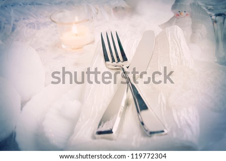 Christmas table setting. Fork and knife in elegant holiday setting with snow and white ornaments