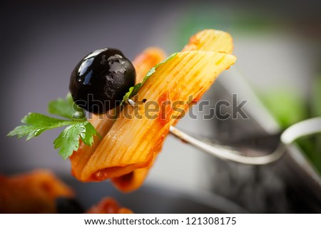 Italian food. Pasta penne with tomato sauce, olives and garnish