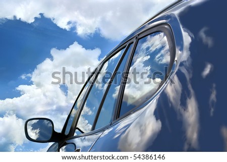 Reflections of the clouds in the polish of the brand new car. Focus is on the front car window. Reflections and the sky create deep palette of blue color in the whole picture.