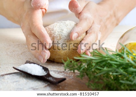 Woman is kneading fresh dough balls in the bakery. Ingredients for dough: salt, olive oil and fresh herbs